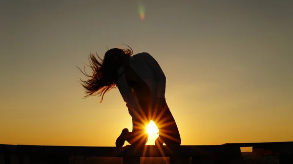 Jeune fille en uniforme de sport assis sur le bord du toit pendant le coucher du soleil . — Photo