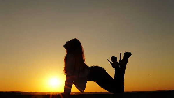 Young girl in sports uniform sits on the edge of the roof during sunset. — Stock Photo, Image