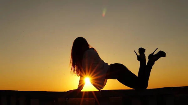 スポーツ制服の少女は、日没時に屋根の端に座っています。. — ストック写真