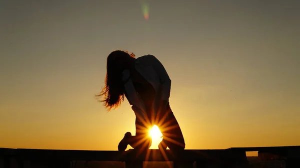 Genç kız spor Tekdüzen çatının kenarında günbatımı sırasında oturur.. — Stok fotoğraf