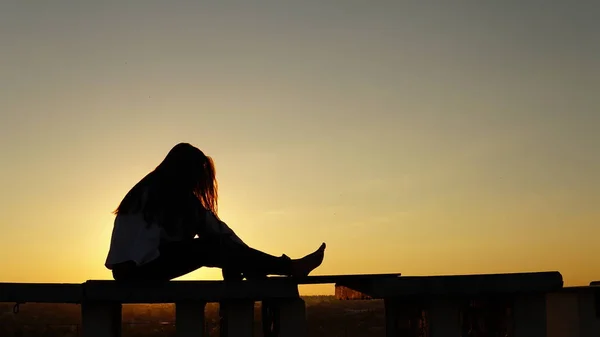 Chica joven en uniforme deportivo se sienta en el borde del techo durante el atardecer . — Foto de Stock