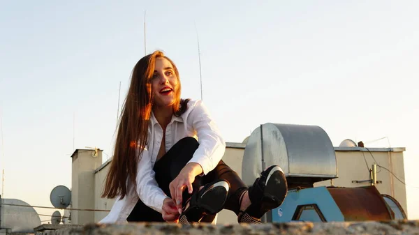 Ung flicka i sport uniform sitter på kanten av taket under solnedgången. — Stockfoto