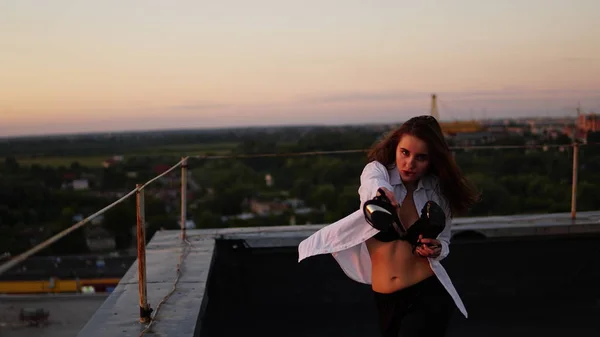 Jong meisje in de sport uniforme zit op de rand van het dak tijdens zonsondergang. — Stockfoto