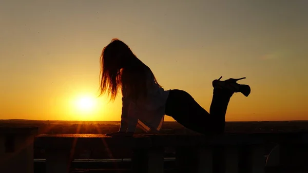 Jeune fille en uniforme de sport assis sur le bord du toit pendant le coucher du soleil . — Photo