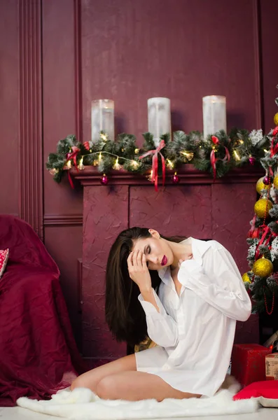 Ritratto di bella ragazza sensualità in camicia jeans, seduta sul letto, in posa, sorridente, rilassante. Loft interno di accogliente camera da letto decorato per Natale e vacanze, notte di festa. Comfort domestico . — Foto Stock