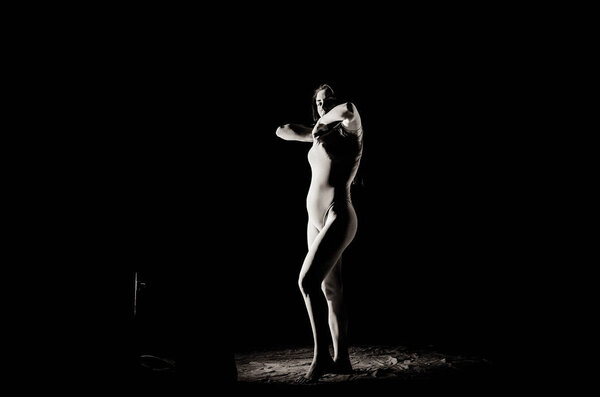 The girl with the flour on the body stretches the arms up with thrown flour on black background black and white image.