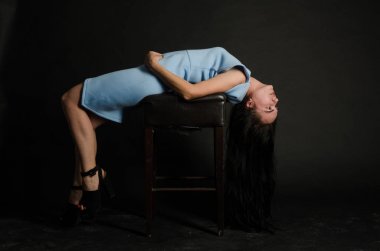 Mavi gece elbisesi poz uzun siyah kıvırcık saçlı genç güzel kadın. Muhteşem çarpıcı kız karanlık iç ayakta. Moda moda tarzı portre.