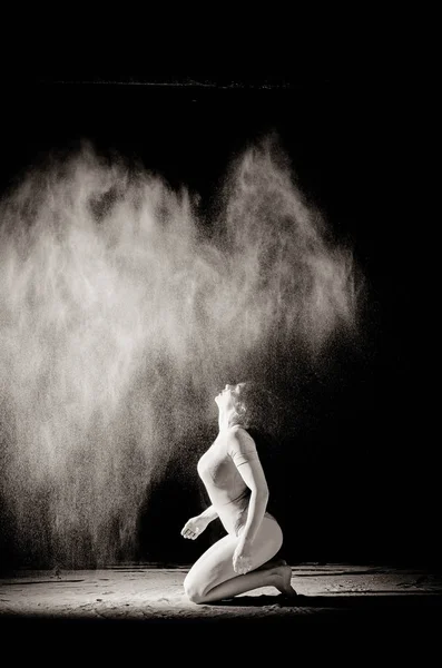 A menina com a farinha no corpo estica os braços com farinha jogada no fundo preto imagem em preto e branco — Fotografia de Stock