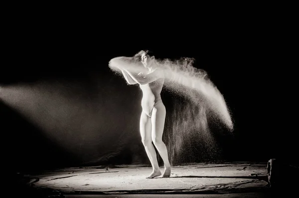 La fille avec la farine sur le corps étire les bras vers le haut avec de la farine jetée sur fond noir image noir et blanc — Photo