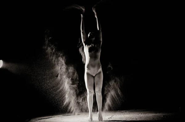 La fille avec la farine sur le corps étire les bras vers le haut avec de la farine jetée sur fond noir image noir et blanc — Photo