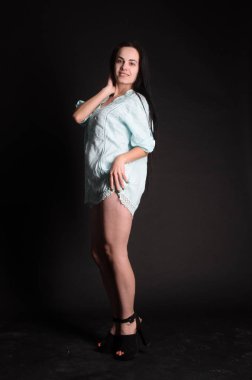 Mavi gece elbisesi poz uzun siyah kıvırcık saçlı genç güzel kadın. Muhteşem çarpıcı kız karanlık iç ayakta. Moda moda tarzı portre.