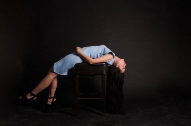 Mavi gece elbisesi poz uzun siyah kıvırcık saçlı genç güzel kadın. Muhteşem çarpıcı kız karanlık iç ayakta. Moda moda tarzı portre.