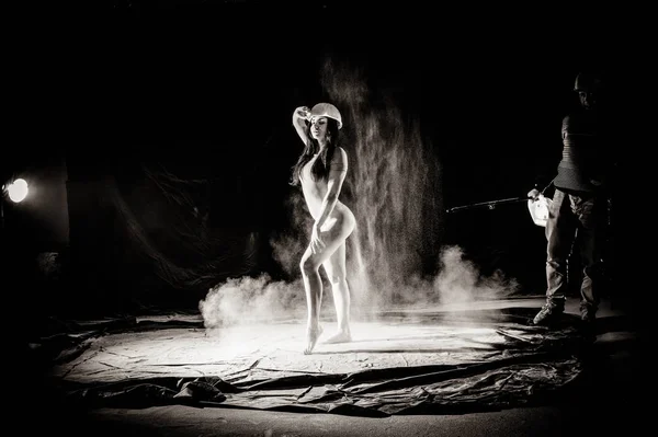 La fille avec la farine sur le corps étire les bras vers le haut avec de la farine jetée sur fond noir image noir et blanc — Photo