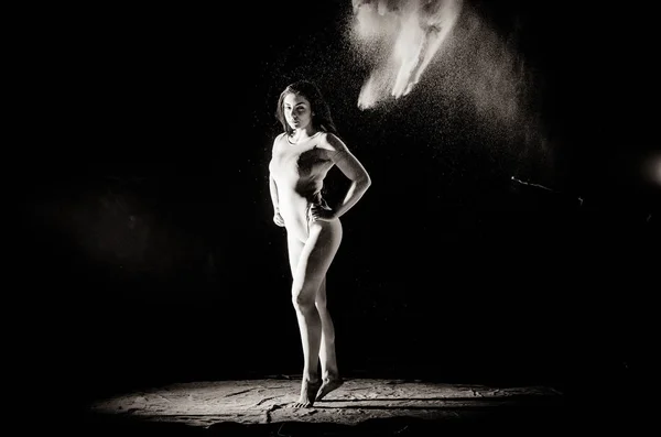 La fille avec la farine sur le corps étire les bras vers le haut avec de la farine jetée sur fond noir image noir et blanc — Photo