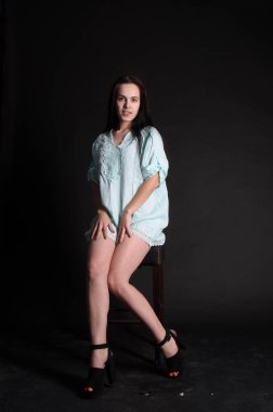 Mavi gece elbisesi poz uzun siyah kıvırcık saçlı genç güzel kadın. Muhteşem çarpıcı kız karanlık iç ayakta. Moda moda tarzı portre.