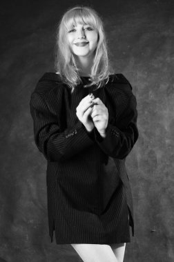 Sandalyeye oturmuş, karanlık stüdyo arka planında poz veren erkek ceketli seksi genç bir kadın. 