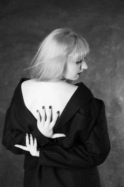 Sandalyeye oturmuş, karanlık stüdyo arka planında poz veren erkek ceketli seksi genç bir kadın. 