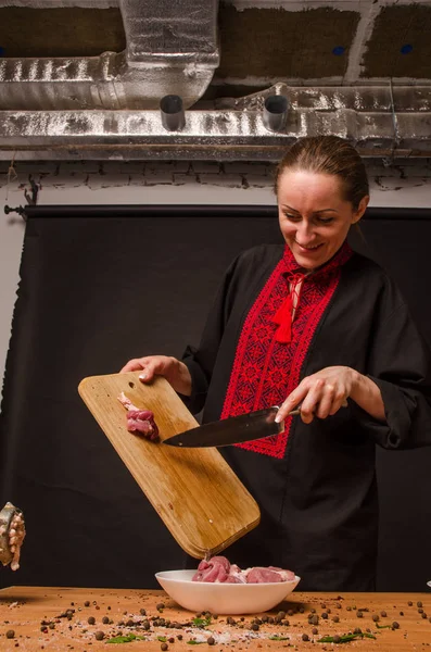 Female chef cuts raw chicken meat on a round wooden Board. The view from the top. Cook chef hands woman cuts raw meat chicken breast on a wooden background