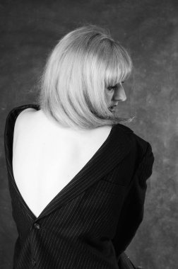 Sandalyeye oturmuş, karanlık stüdyo arka planında poz veren erkek ceketli seksi genç bir kadın. 