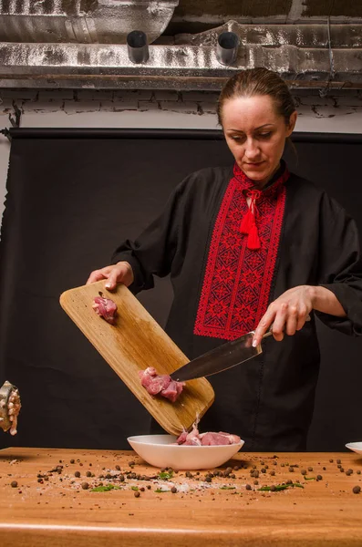 Female chef cuts raw chicken meat on a round wooden Board. The view from the top. Cook chef hands woman cuts raw meat chicken breast on a wooden background