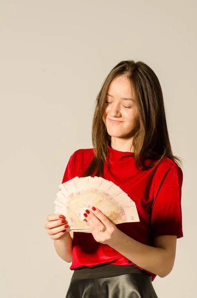 Eine sexy Brünette in einem kurzen Rock auf hellem Hintergrund zählt Geld. — Stockfoto