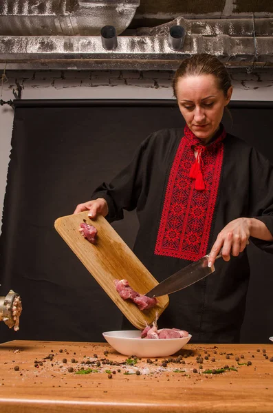 Female chef cuts raw chicken meat on a round wooden Board. The view from the top. Cook chef hands woman cuts raw meat chicken breast on a wooden background
