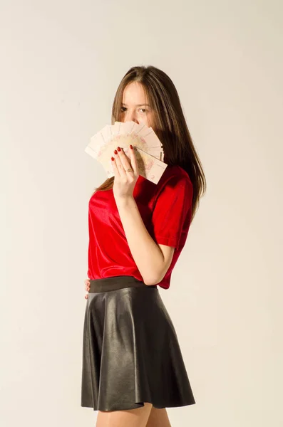 En sexig brunett i kort kjol på en ljus bakgrund räknas pengar. — Stockfoto