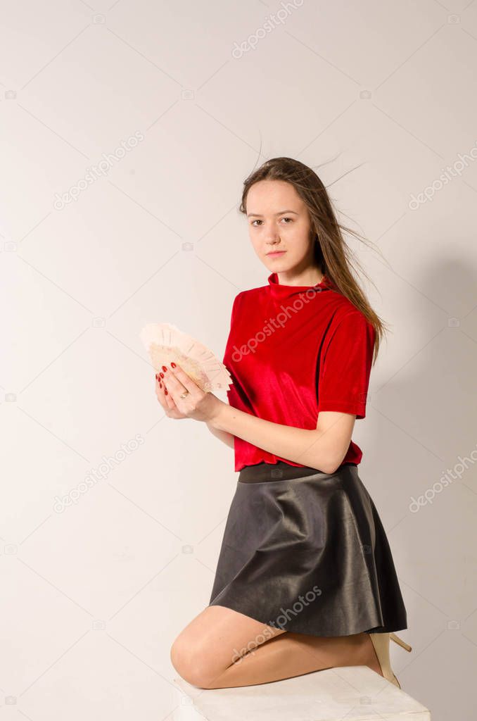 A sexy brunette in a short skirt on a light background counts money.