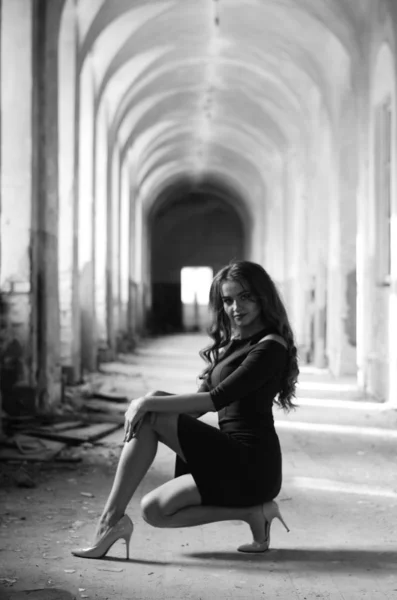 Young beautiful short hair blonde woman in black climbing the stairs, black and white photo. Side view of elegant romantic mysterious lady with movie star look in interior with bricks walls — Stock Photo, Image