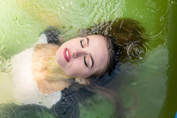 Hermosa modelo femenina vestida con largos vestidos de noche, se encuentra en la piscina y plantea sensualmente — Foto de Stock