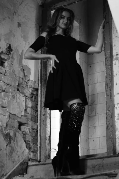 Young beautiful short hair blonde woman in black climbing the stairs, black and white photo. Side view of elegant romantic mysterious lady with movie star look in interior with bricks walls — Stock Photo, Image