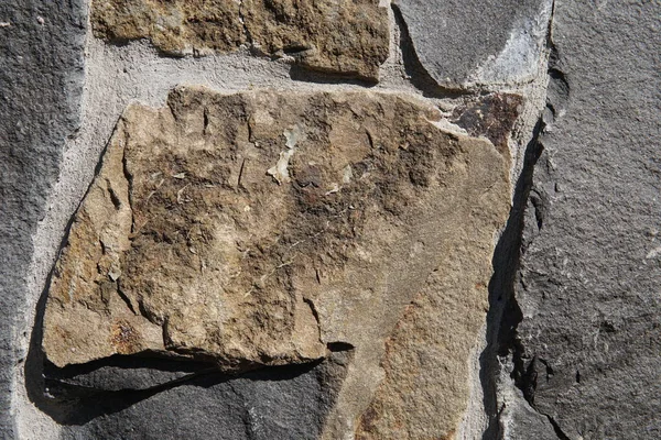 Decorative wall of artificial torn stone in brown tones. Stone masonry in geometric pattern as background or texture.