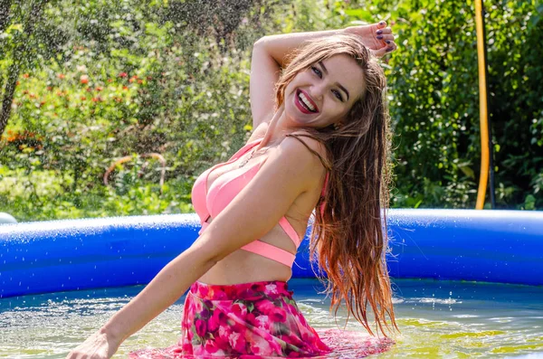 Beautiful blonde woman model with amazing body standing in the pool in an elegant red swimsuit and in the background is amazing view of the sea and sky. — Stock Photo, Image