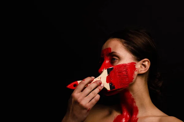 Retrato criativo de uma jovem. O rosto é pintado com tinta vermelha brilhante. O triângulo é desenhado no rosto. Modelo em perfil sobre fundo preto — Fotografia de Stock