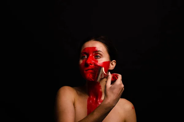 Retrato criativo de uma jovem. O rosto é pintado com tinta vermelha brilhante. O triângulo é desenhado no rosto. Modelo em perfil sobre fundo preto — Fotografia de Stock