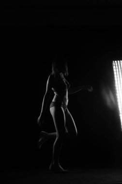 Kısa donlu güzel bir kadın silueti. Karanlık stüdyo arka planında poz veriyor.    