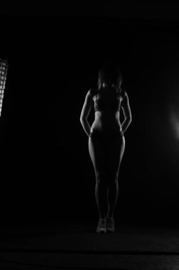 Kısa donlu güzel bir kadın silueti. Karanlık stüdyo arka planında poz veriyor.    