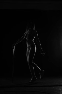 Kısa donlu güzel bir kadın silueti. Karanlık stüdyo arka planında poz veriyor.    