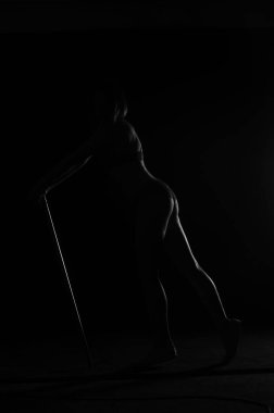 Kısa donlu güzel bir kadın silueti. Karanlık stüdyo arka planında poz veriyor.    