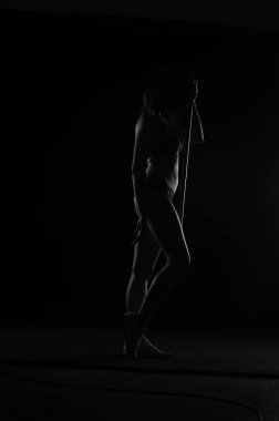 Kısa donlu güzel bir kadın silueti. Karanlık stüdyo arka planında poz veriyor.    