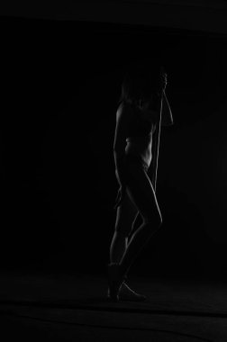 Kısa donlu güzel bir kadın silueti. Karanlık stüdyo arka planında poz veriyor.    