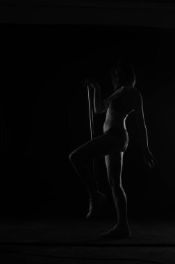 Kısa donlu güzel bir kadın silueti. Karanlık stüdyo arka planında poz veriyor.    
