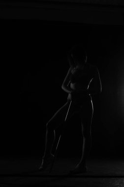 Kısa donlu güzel bir kadın silueti. Karanlık stüdyo arka planında poz veriyor.    