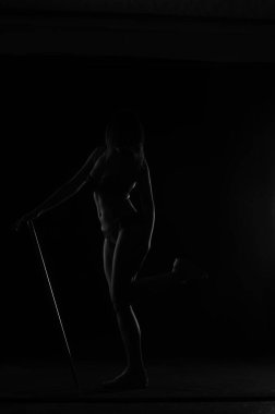 Kısa donlu güzel bir kadın silueti. Karanlık stüdyo arka planında poz veriyor.    