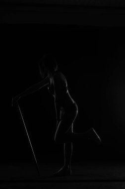 Kısa donlu güzel bir kadın silueti. Karanlık stüdyo arka planında poz veriyor.    