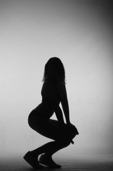 Silhouette of beautiful woman with short hear in lingerie posing on light studio background