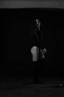 beautiful brunette young woman in black bodysuit posing on dark studio background 