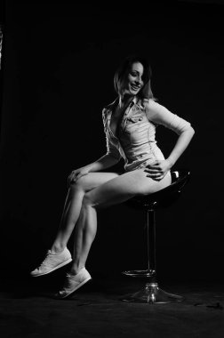 Kısa boylu, şık giyinen, karanlık stüdyo arka planında poz veren güzel kadın.  