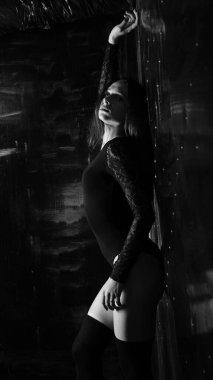 Siyah elbiseli genç bir kadın koyu bir arka planda poz veriyor, siyah saçlı ve kaslı bir spor figürü..