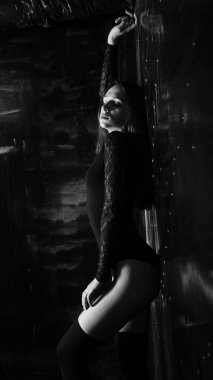 Siyah elbiseli genç bir kadın koyu bir arka planda poz veriyor, siyah saçlı ve kaslı bir spor figürü..